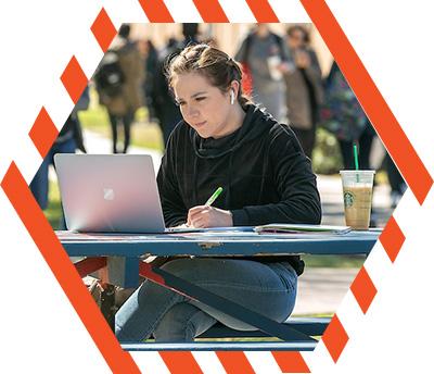 student taking notes while studying on a picnic table with laptop open